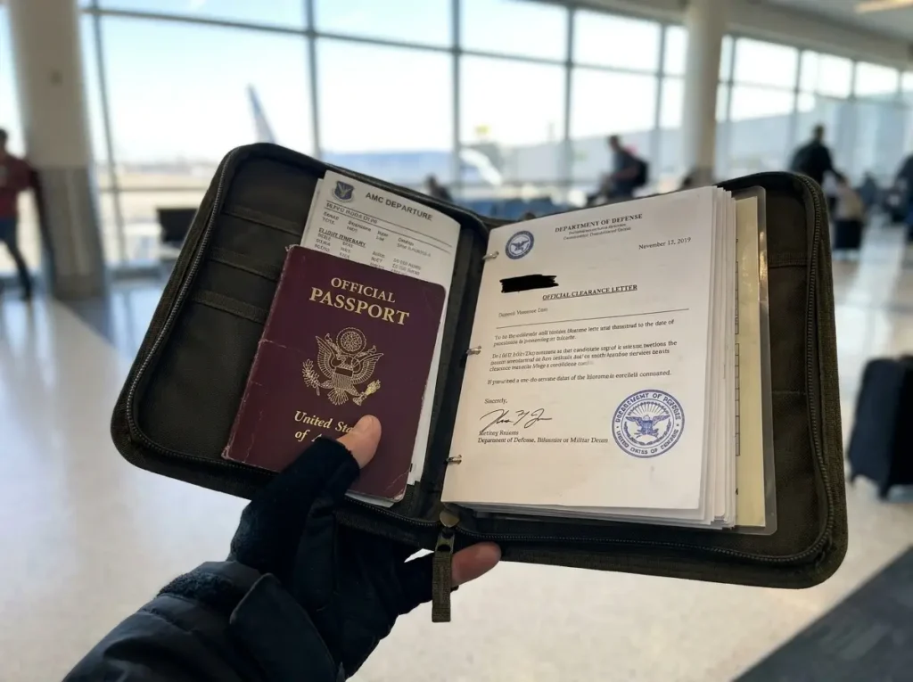 A close-up of an open travel folder containing a maroon No-Fee passport, an official stamped letter, and a flight itinerary at a busy airport, illustrating exactly what to put in a PCS binder for an overseas military move.