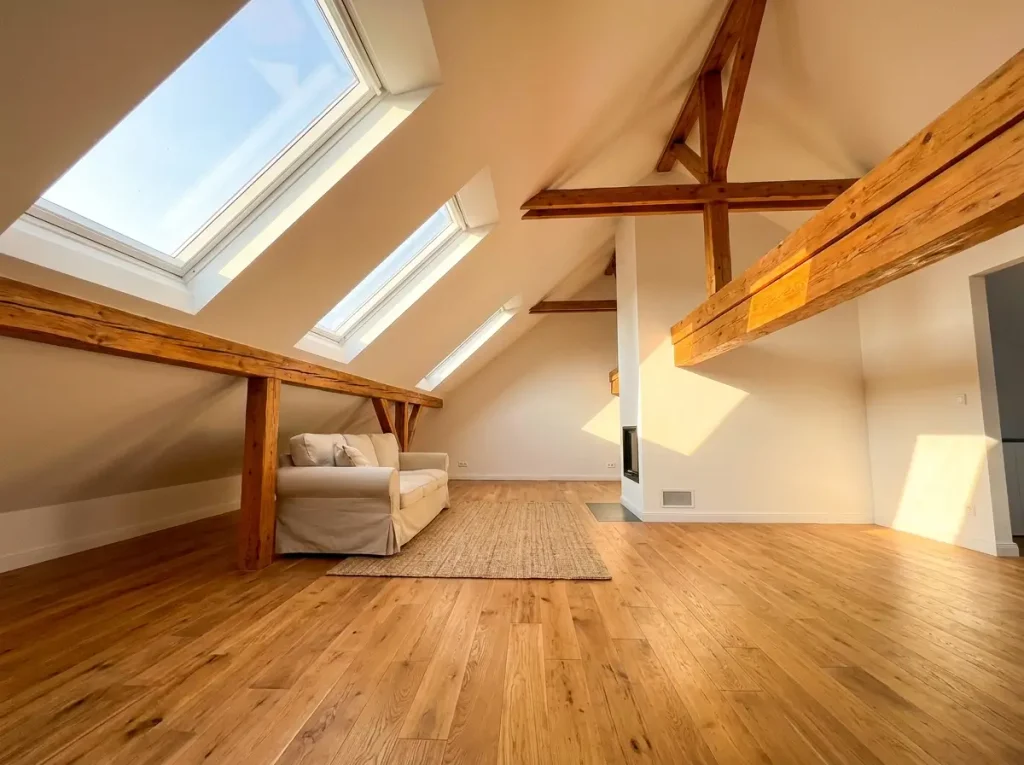 A beautifully renovated, sunlit attic featuring large skylights and exposed wooden beams, providing inspiring small loft ideas for an architectural conversion.